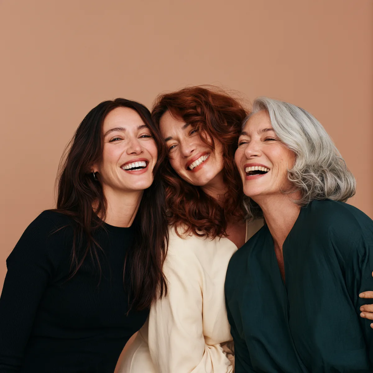 Three women of different ages leaning together and laughing, one holding a small glass of liquid collagen
