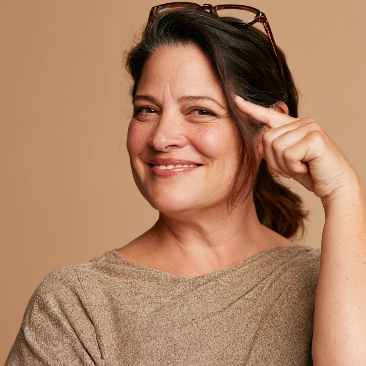 Woman in her forties holding an amber pack of liquid collagen beside her face and pointing at it, smiling
