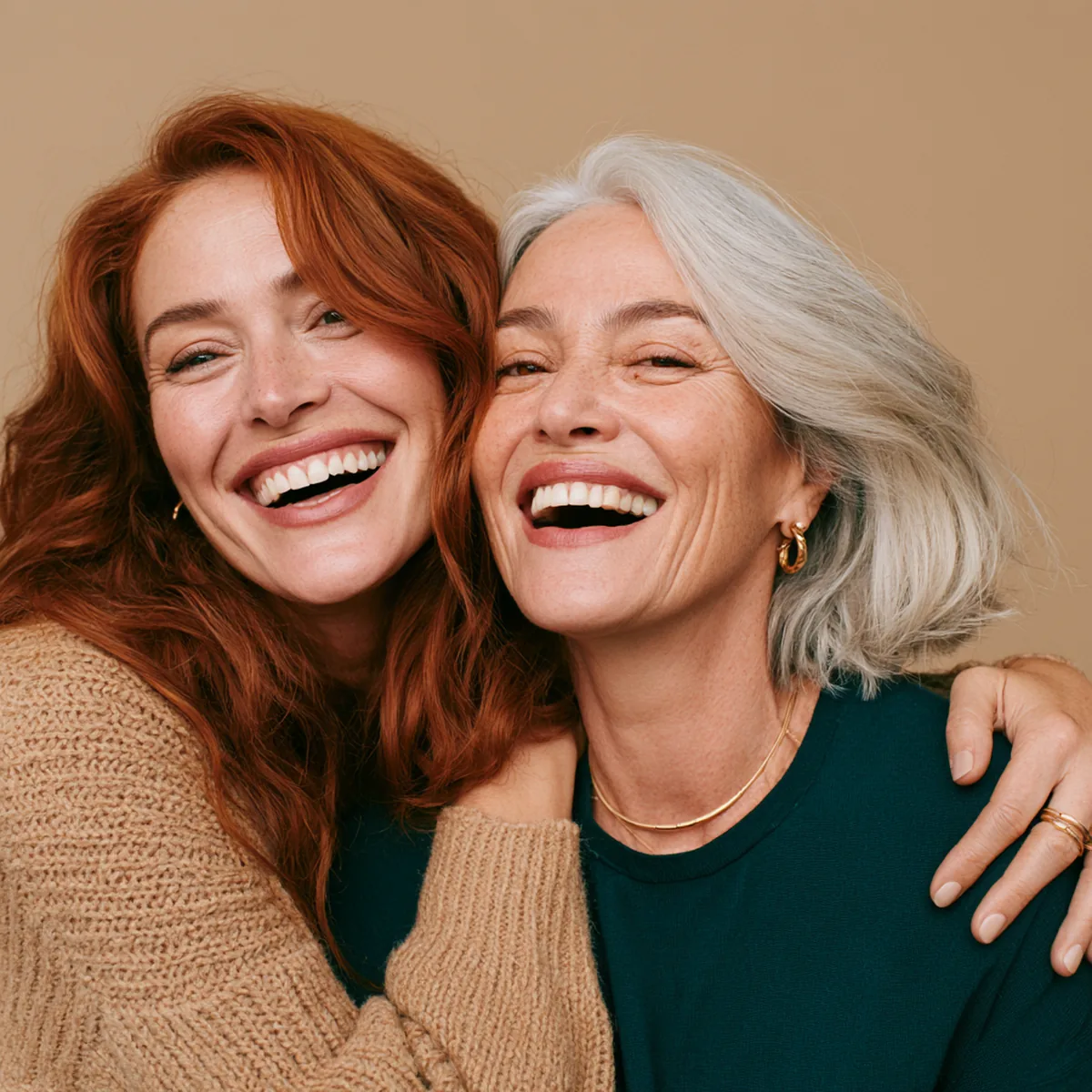 Two women with auburn and silver hair laughing arm in arm, each holding a small glass of berry-red drink