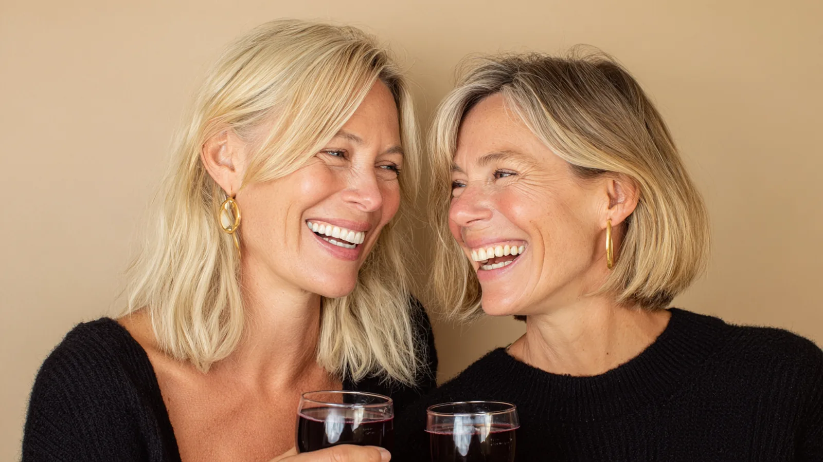 Two women in their forties and fifties laughing and clinking small glasses of berry-red liquid collagen