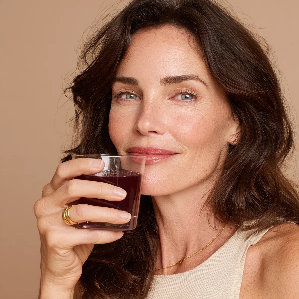 Brunette woman in her forties tipping a measuring cap of berry-red liquid collagen towards her lips
