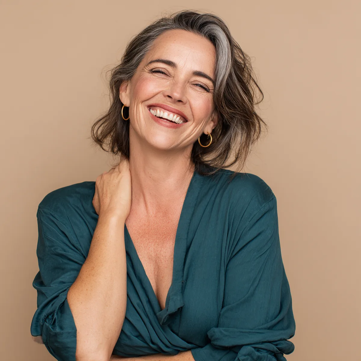 Confident woman in her fifties with silver-streaked hair laughing openly in a deep teal top