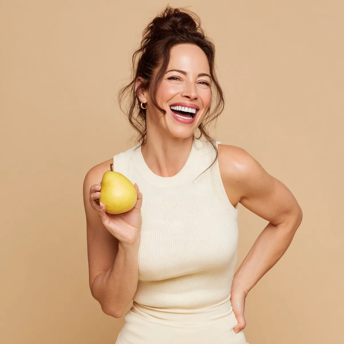 Laughing woman in her forties flexing one arm playfully and holding a ripe pear in the other hand