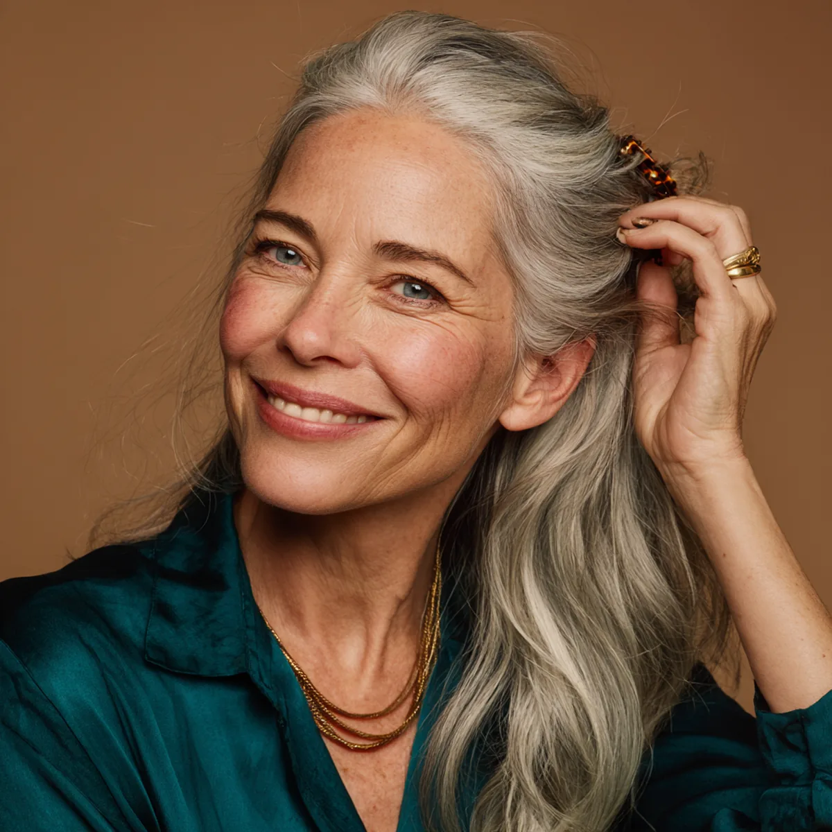 Woman in her fifties with silver hair running her fingers through it and smiling, in a deep teal blouse