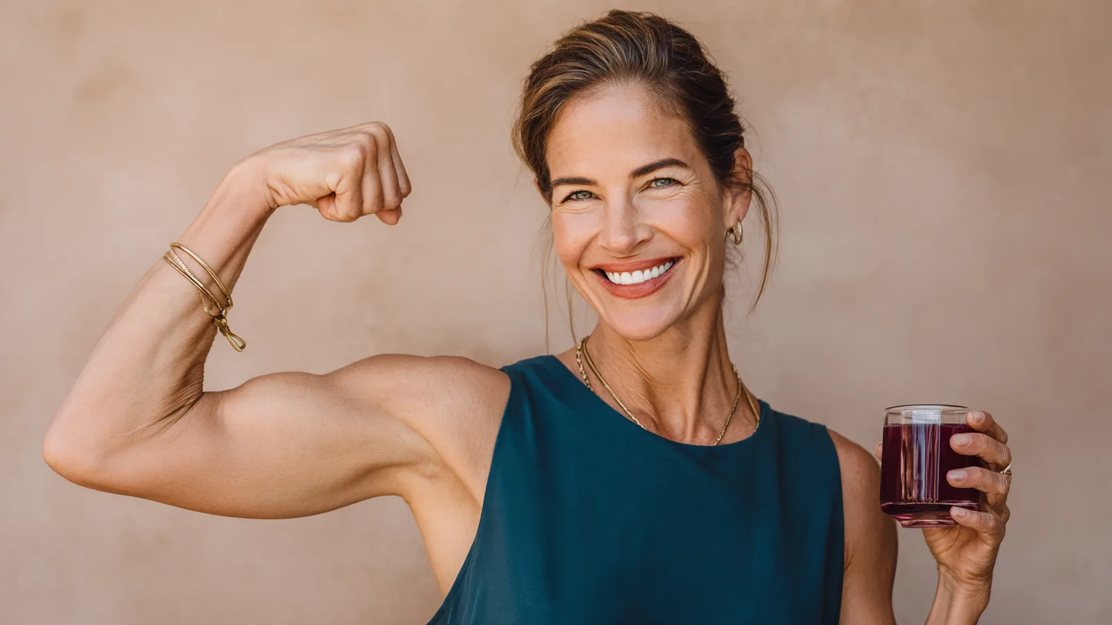 Woman in her forties playfully flexing one arm and raising a small glass of collagen protein drink