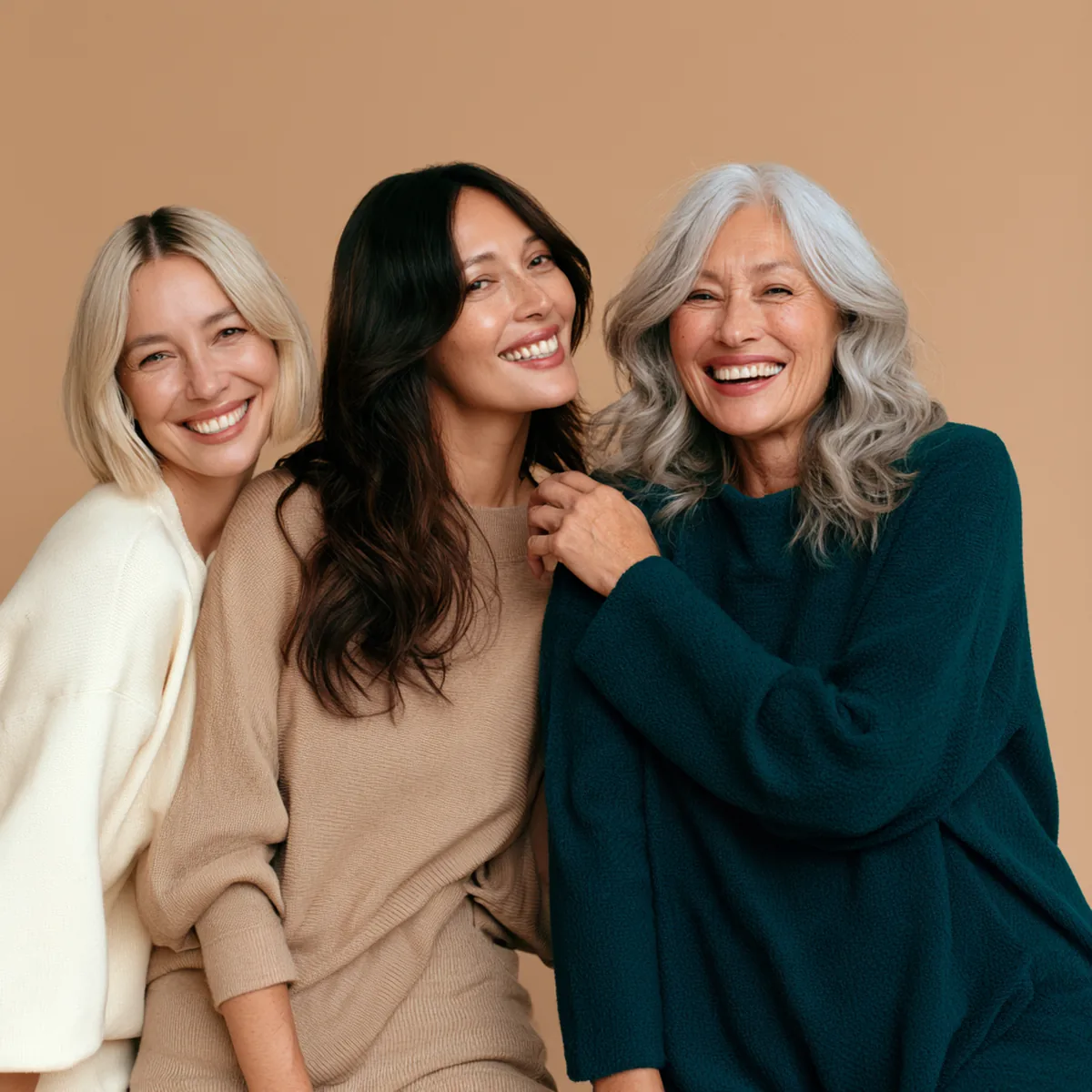 Three women in their forties and fifties laughing together, one holding up a small glass of berry-red collagen drink
