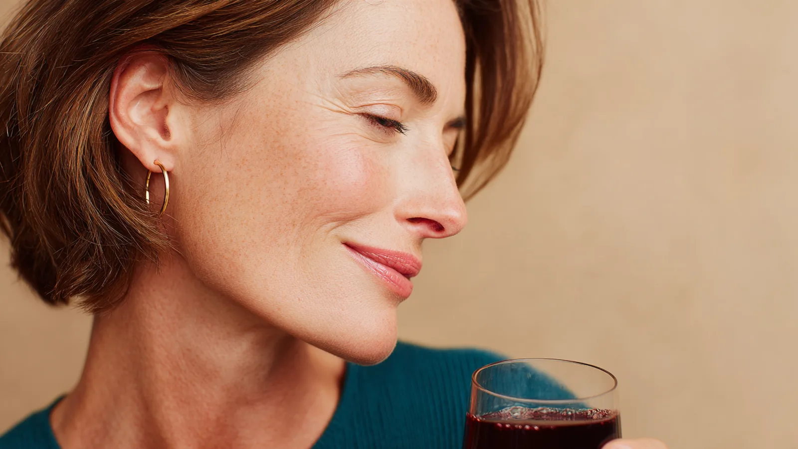 Side view of a smiling woman's cheek and jawline with bare skin, a small drink held near her chin