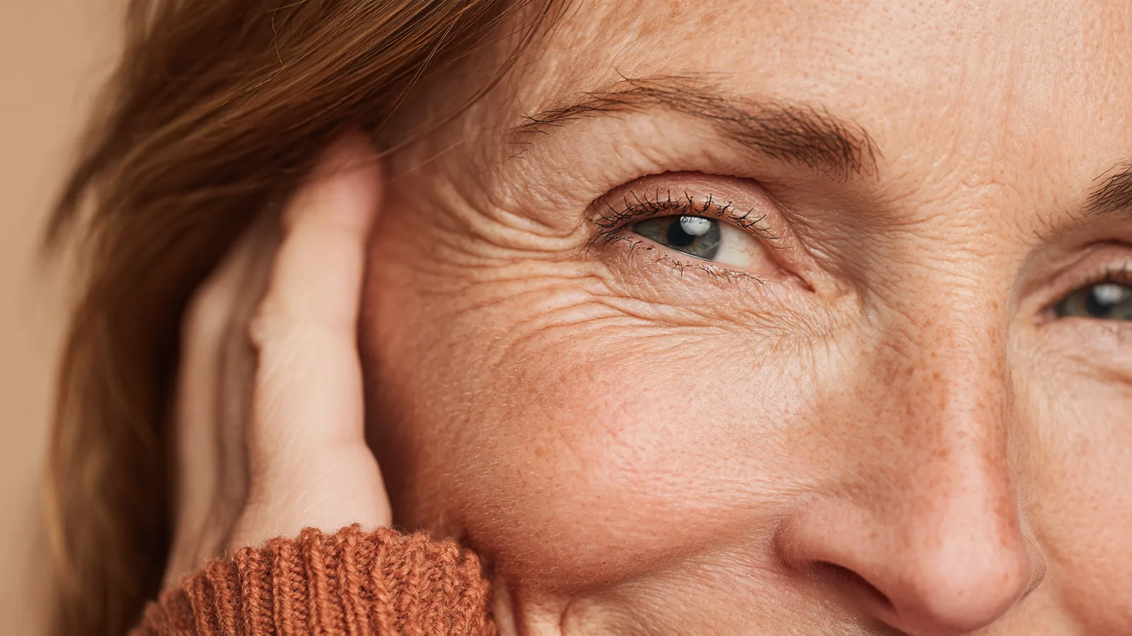 Close view of a smiling woman's eye and cheek, soft natural lines and dewy, healthy skin